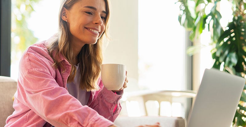 Smiling woman on laptop drinking from mug